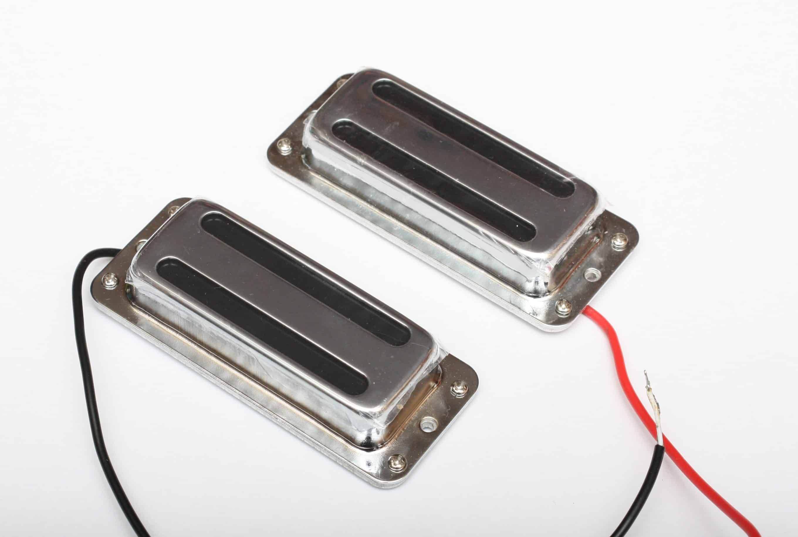 Two chrome electric guitar pickups with black covers and exposed red and black wires on a white background