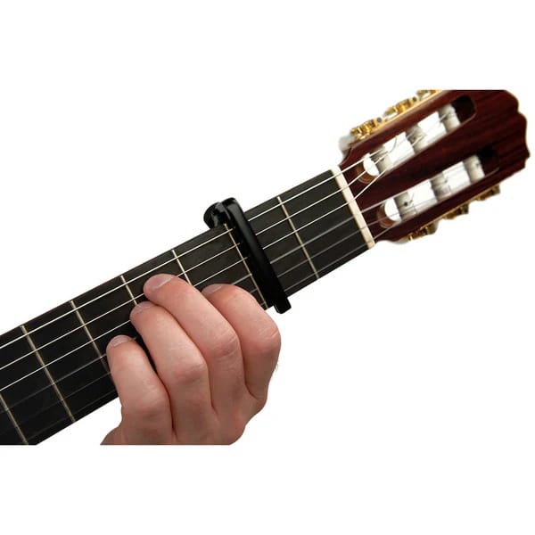 Close-up of a hand placing a black capo on the fretboard of a classical guitar, near the headstock
